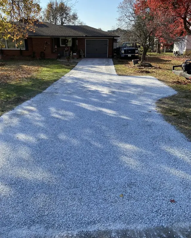 Light stone chip seal driveway at a brick ranch home with a red maple in fall color