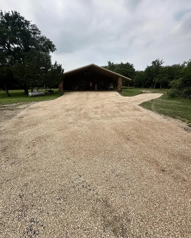 Wide tan chip seal drive leading to a timber pavilion under oak trees