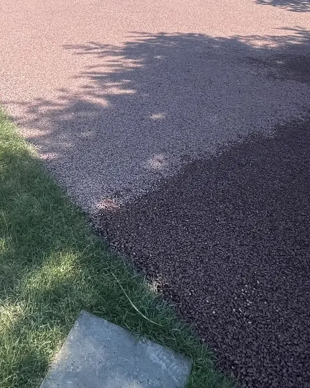 Close view of a red stone chip seal surface meeting the lawn in dappled tree shade